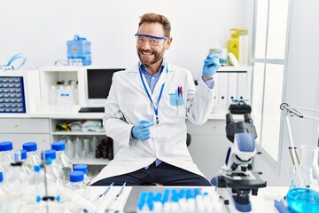 Fototapeta premium Middle age man working at scientist laboratory smiling happy pointing with hand and finger to the side