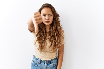 Beautiful hispanic woman standing over isolated while background looking unhappy and angry showing rejection and negative with thumbs down gesture. bad expression.