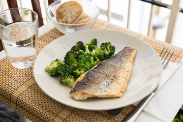 fried fillet of sea bass with garnish of broccoli on black warm stone plate