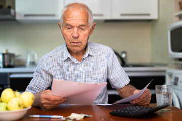Elderly man sitting in kitchen with utility bills