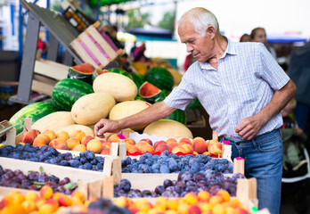 retired european man buying plums peaches nectarine in market