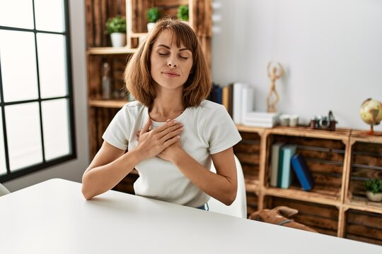 Young caucasian girl wearing casual clothes sitting on the table at home smiling with hands on chest with closed eyes and grateful gesture on face. health concept.