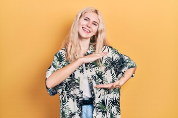 Beautiful caucasian woman with blond hair wearing tropical shirt gesturing with hands showing big and large size sign, measure symbol. smiling looking at the camera. measuring concept.