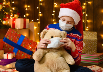 Child girl as Santa helper posing in new year decoration. Wearing a protective face mask against...