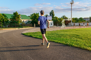 concept of sports and health - teen boy runs along the stadium track, a soccer field with green...