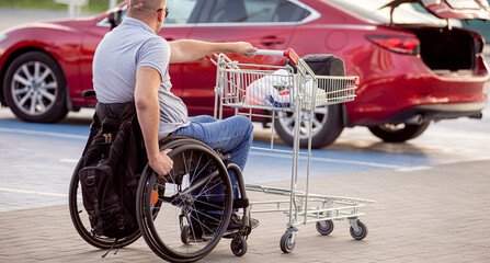 Fototapeta na wymiar Person with a physical disability pushes a cart towards a car in a supermarket parking lot