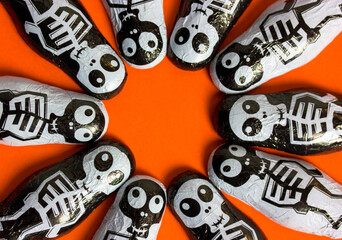 Trick or treat chocolate candies in the shape of black and white skeletons on orange background with round frame for text inside it. Halloween sweets and treats. October 31st. Funny scary characters