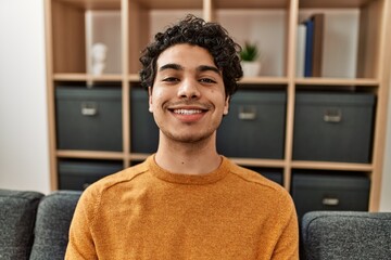 Young hispanic man smiling happy sitting on the sofa at home.