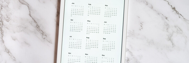 tablet computer with an open app of calendar for unspecified date year without date on a gray marble background. concept business or to do list goals with technology using. top view, flat lay. banner