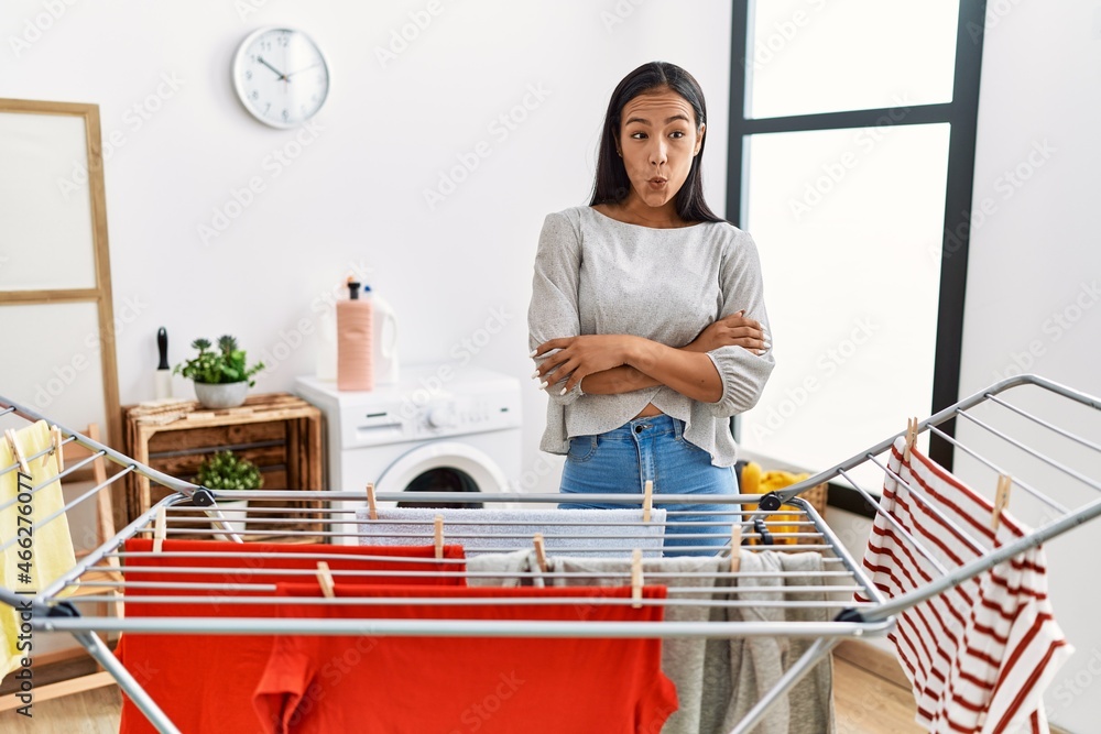 Sticker young hispanic woman putting fresh laundry on clothesline afraid and shocked with surprise expressio