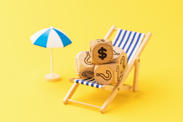 Wooden toy cubes with dollar symbol and question mark in deck chair and parasol on yellow...