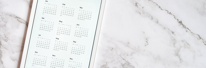 tablet computer with an open app of calendar for unspecified date year without date on a gray marble background. concept business or to do list goals with technology using. top view, flat lay. banner
