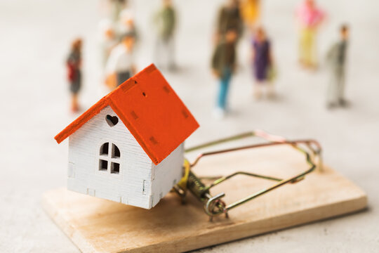 A toy house in a mousetrap on the background of people, a concept on the topic of real estate fraud
