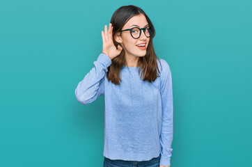 Young beautiful woman wearing casual clothes and glasses smiling with hand over ear listening an hearing to rumor or gossip. deafness concept.