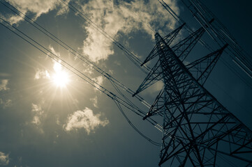 An electricity pylon stands tall in the hot summer sun with a few wispy clouds. Solar Power concept.