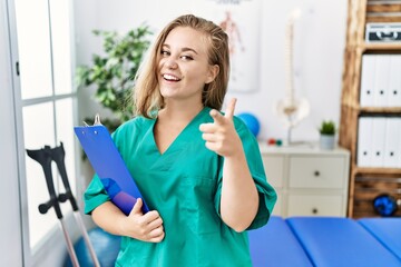 Young caucasian woman working at pain recovery clinic pointing fingers to camera with happy and funny face. good energy and vibes.