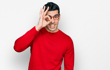Fototapeta premium Handsome hispanic man wearing casual clothes and glasses doing ok gesture with hand smiling, eye looking through fingers with happy face.