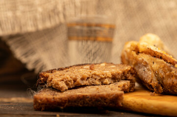 A small fried fish on a wooden board, pieces of bread and a glass of vodka, close-up, selective focus.