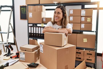 Young hispanic woman smiling confident leaning on delivery package at store