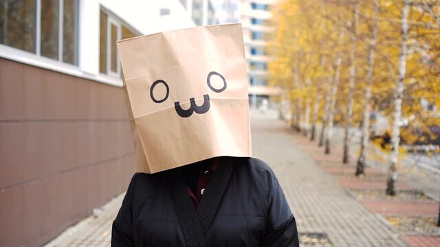 Funny paper bag face walking along street. Portrait of woman in bread bag on which cat are drawn