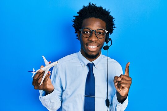Young african american travel agent man holding plane smiling with an idea or question pointing finger with happy face, number one