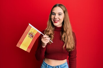 Young blonde woman holding spain flag looking positive and happy standing and smiling with a confident smile showing teeth