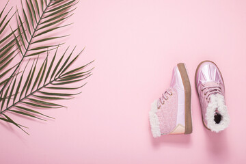 Boots for a girl, a leaf of a palm tree on a pink background. Top view, flat lay.
