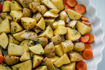 Oven baking vegetables in baking dish, potatoes and carrots with spicy herbs, homemade vegan vegetable dish recipe background