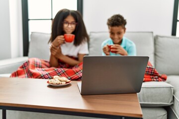 Brother and sister having breakfast watching movie sitting on sofa at home