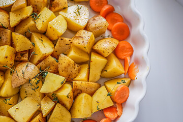 Oven baking vegetables in baking dish, potatoes and carrots with spicy herbs, homemade vegan vegetable dish recipe background