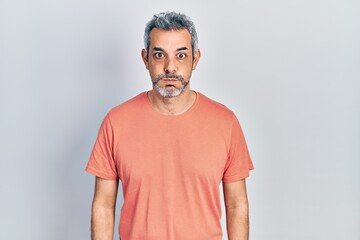 Handsome middle age man with grey hair wearing casual t shirt puffing cheeks with funny face. mouth...