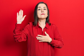 Middle age hispanic woman wearing casual clothes swearing with hand on chest and open palm, making...