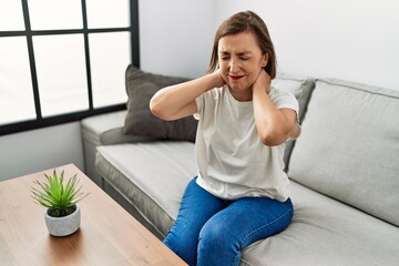 Middle age hispanic woman sitting on the sofa with neck pain at home