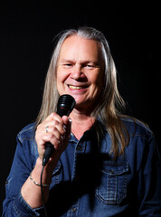 elderly man with long gray hair sings into a microphone