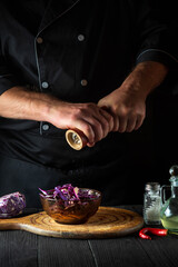 Professional chef adds pepper to a fresh red cabbage salad. Cooking healthy food in restaurant kitchen on vintage table.