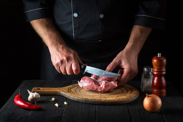 Chef cuts meat with a knife in the kitchen prepares food. Vegetables and spices on kitchen table in a restaurant to prepare delicious lunch