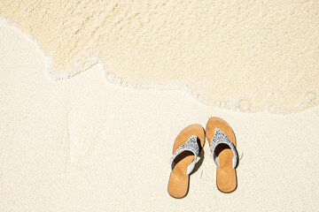 Summer white flop flops or sandals on sandy beach by sea water, top view, copy space