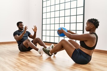 Young african american sporty couple doing abs exercise using ball at sport center.