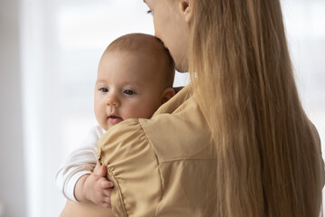 Rear view close up loving young mother holding adorable newborn baby in arms, kissing in head, family enjoying tender moment, happy mom hugging little child kid, motherhood and childcare concept