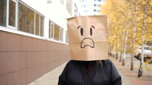 Frightened paper bag face with open mouth walking along street.