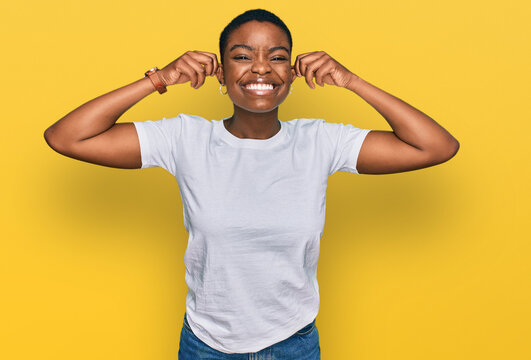 Young african american woman wearing casual white t shirt smiling pulling ears with fingers, funny gesture. audition problem