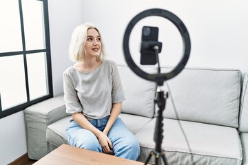 Young caucasian woman recording vlog tutorial with smartphone at home looking away to side with smile on face, natural expression. laughing confident.