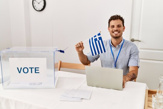 Young hispanic man smiling confident holding greece flag working at electoral college