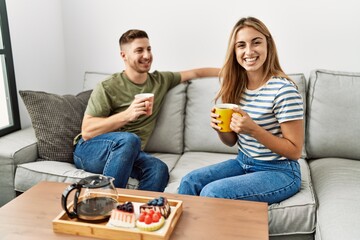 Obraz premium Young hispanic couple smiling happy having breakfast sitting on the sofa at home.