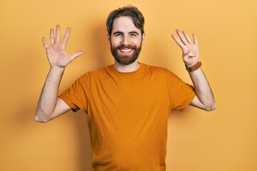 Caucasian man with beard wearing casual yellow t shirt showing and pointing up with fingers number...