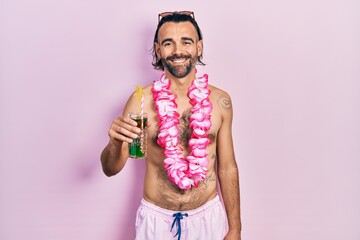 Young hispanic man wearing swimsuit and hawaiian lei drinking tropical cocktail with a happy and...