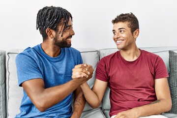 Two men friends smiling confident shake hands sitting on sofa at home