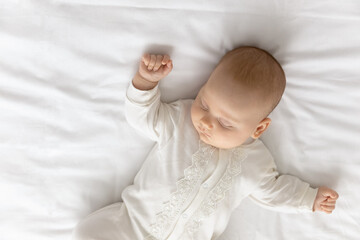 Top view close up cute Caucasian baby in white bodysuit sleeping, adorable newborn child with closed eyes lying on comfortable bed, relaxing, dreaming resting alone, fall asleep, childhood concept