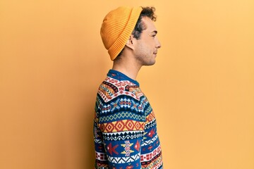 Young handsome man wearing wool hat and colorful sweater looking to side, relax profile pose with...