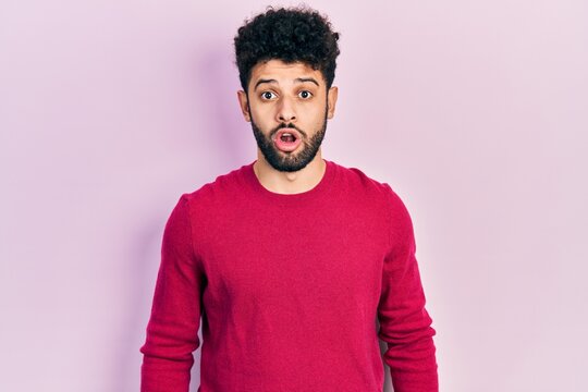Young arab man with beard wearing casual pink sweater scared and amazed with open mouth for surprise, disbelief face